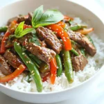 - 1 lb (450g) beef sirloin, thinly sliced - 2 cups fresh Thai basil leaves - 1 red bell pepper, thinly sliced - 1 cup green beans, trimmed and halved - 4 cloves garlic, minced - 2 tablespoons soy sauce - 1 tablespoon oyster sauce - 1 tablespoon fish sauce - 1 tablespoon brown sugar - 1 teaspoon chili flakes (adjust to taste) - Large skillet or wok - Cooking spoon - Cutting board - Knife - Small bowl for sauce mixing Gather these items before you start cooking. The fresh Thai basil gives the dish its unique flavor. The beef sirloin adds a nice texture. You can use other veggies, but I love red bell pepper and green beans. They make the dish colorful and tasty. Make sure to have all the sauces ready. They blend well and boost the flavor. A large skillet or wok is best for stir-frying. It helps cook everything evenly. Now that you have your ingredients, you're ready to make a delicious Thai basil beef stir fry! {{ingredient_image_1}} Start by slicing the beef sirloin thinly. This helps it cook fast and evenly. Aim for slices about a quarter-inch thick. Thin slices absorb flavors well. Set the beef aside on a plate while you prepare the rest. Heat your skillet or wok over high heat. Add vegetable oil and let it shimmer. Once hot, add minced garlic. Stir for about 30 seconds until it smells good. Don’t let it burn! Next, add the beef slices. Spread them out in a single layer. Let them sear for 2 minutes. Then stir-fry for 2 to 3 minutes until the beef turns brown and is fully cooked. Now, it’s time for the veggies! Add sliced red bell pepper and green beans to the skillet. Stir-fry these for 2 to 3 minutes. You want them tender but still a bit crisp. In a small bowl, mix soy sauce, oyster sauce, fish sauce, and brown sugar. Pour this sauce over the beef and veggies. Stir well to coat everything nicely. For a bit of heat, add chili flakes. Finally, toss in the fresh Thai basil leaves. Stir for another minute until everything is mixed well. Serve hot over jasmine rice. Enjoy your meal! To get a great sear, use high heat. Heat the vegetable oil until it shimmers. Spread the beef in a single layer. Let it sit without stirring for two minutes. This helps create a nice crust. After that, stir-fry for another two to three minutes. Your beef should be browned and juicy. You can control the heat in this dish easily. Start with one teaspoon of chili flakes. If you like it hot, add more while cooking. Taste the dish before serving. This way, you can adjust the spice to fit your taste. When choosing Thai basil, look for bright green leaves. They should be firm and not wilted. A strong, sweet smell is a good sign. Avoid any leaves that have brown spots. Fresh basil will make your dish pop with flavor. Pro Tips Tip Title: Use Fresh Ingredients: Fresh Thai basil and crisp vegetables enhance the flavor and texture of your stir fry. Tip Title: Don't Overcrowd the Pan: To achieve a nice sear on the beef, cook in batches if necessary to avoid steaming. Tip Title: Adjust Spice Level: Feel free to modify the amount of chili flakes according to your heat preference. Tip Title: Serve Immediately: For the best taste and texture, serve the stir fry right after cooking while it's hot. {{image_2}} You can easily swap beef for other proteins. Chicken or shrimp work great. For a vegetarian option, try tofu. Make sure to press the tofu to remove extra water. This helps it absorb flavors better. Feel free to mix up the veggies. Broccoli, snap peas, or carrots add nice crunch. You can even use mushrooms for a savory twist. Use whatever you have on hand. This dish is flexible! To make this dish lighter, use less oil. You can replace brown sugar with a sugar substitute. Choose a low-sodium soy sauce for less salt. Adding more vegetables can boost fiber too. Enjoy a tasty meal without compromising health! After enjoying your Thai basil beef stir fry, let the leftovers cool. Place them in an airtight container. Store them in the fridge for up to three days. This keeps the flavors fresh and tasty. If you want to save them longer, consider freezing. When you're ready to eat the leftovers, reheat them in a skillet. Use low to medium heat for even warming. Stir the mixture to ensure it heats through. You can also use a microwave. Heat it in 30-second intervals, stirring between each. This helps avoid hot spots and keeps the beef juicy. To freeze your stir fry, place it in a freezer-safe bag or container. Remove as much air as you can. Proper storage prevents freezer burn. You can keep it frozen for up to three months. When you want to enjoy it, thaw it overnight in the fridge. Then, reheat it in a skillet or microwave as mentioned above. This makes for a quick and tasty meal later on. You can serve Thai Basil Beef Stir Fry with cooked jasmine rice. The rice absorbs the tasty sauce. You might also add a side of steamed broccoli or a fresh cucumber salad. These options balance the meal and add freshness. If you like, a light soup can also pair well. Yes, you can make this dish in advance. Cook the stir fry and cool it down. Store it in an airtight container in the fridge. It will stay good for about three days. When you are ready to eat, just reheat it on the stove. This dish tastes great even after a day. Yes, Thai Basil is different from regular basil. Thai Basil has a spicier and more fragrant flavor. Its leaves are darker and have a slight purple hue. Regular basil, like sweet basil, has a sweeter taste. Both can work in cooking, but Thai Basil is best for this dish. This blog post covered how to make Thai Basil Beef Stir Fry. We looked at the key ingredients, step-by-step instructions, and helpful tips. I shared ideas for variations and how to store your dish. Remember, stir-frying is quick and fun. With fresh ingredients and some practice, you can enjoy this meal whenever you want. Cooking at home brings joy and creativity. Try these methods, and flavor will follow. Enjoy your time in the kitchen!